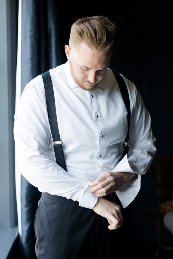 groom prepping on his wedding day in black an white suspender tux