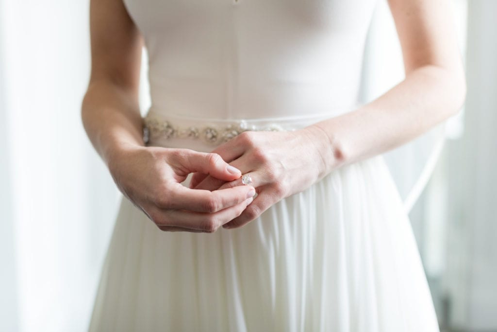 bride putting on her round engagement ring