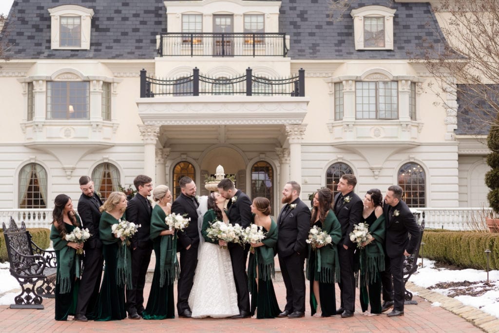 bride and groom kissing with their wedding party watching