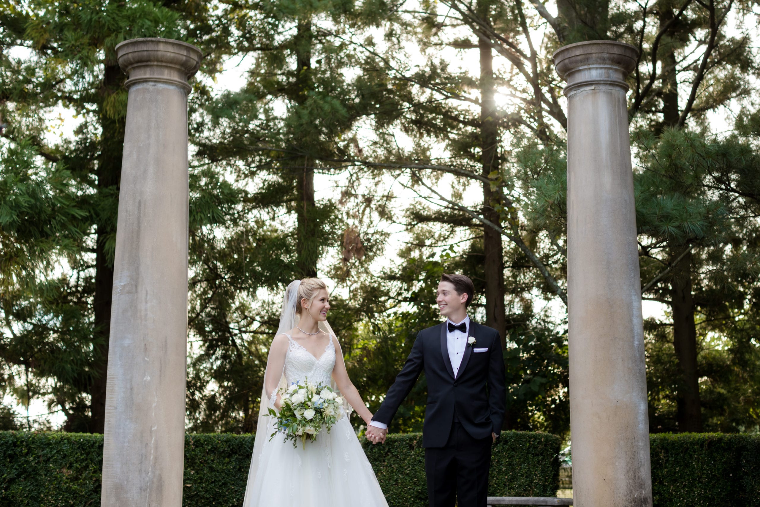Bride and groom holding hands between two stone columns with pine trees behind