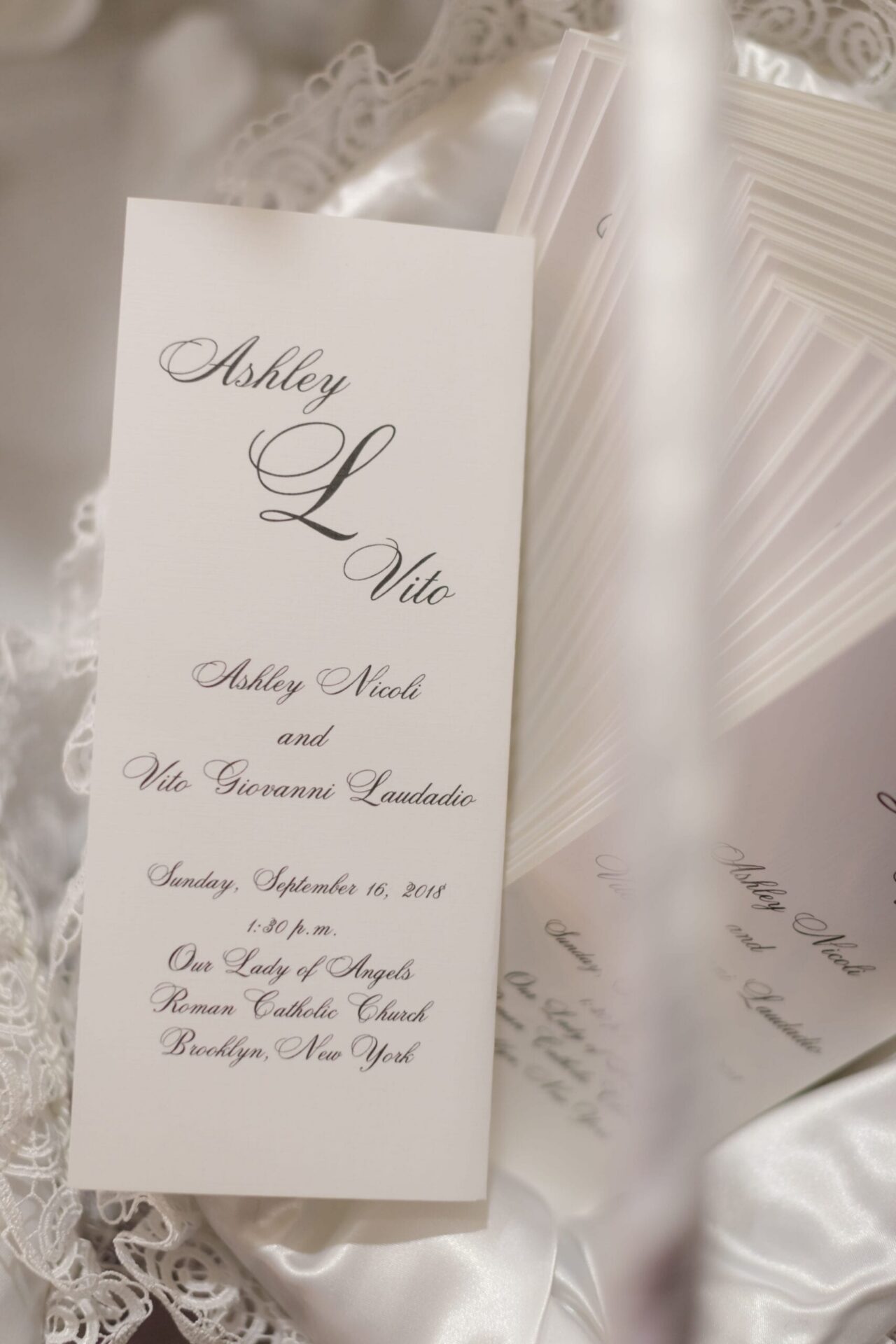 Folded ceremony program in script lettering resting on lace and satin
