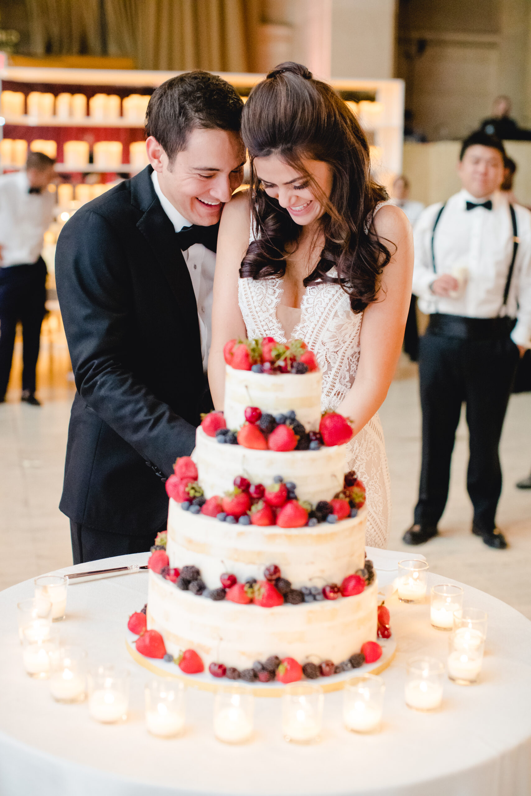 Bride and groom laughing as they cut a naked cake topped with berries