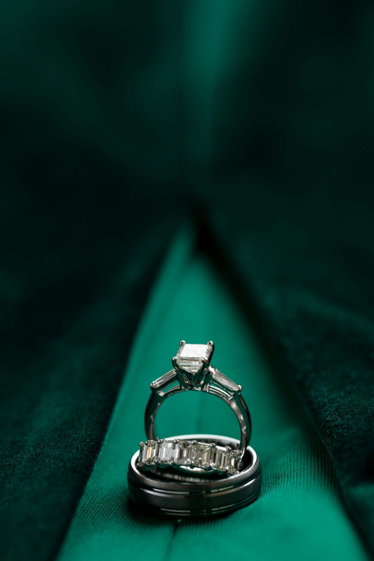 Emerald-cut engagement ring and wedding bands on bright green velvet