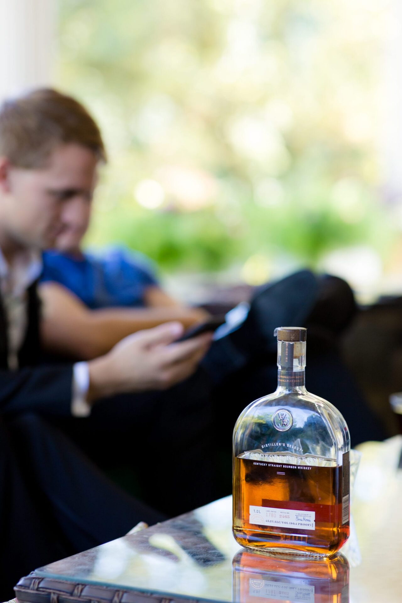 Groomsman checking a phone beside a bourbon bottle on a table