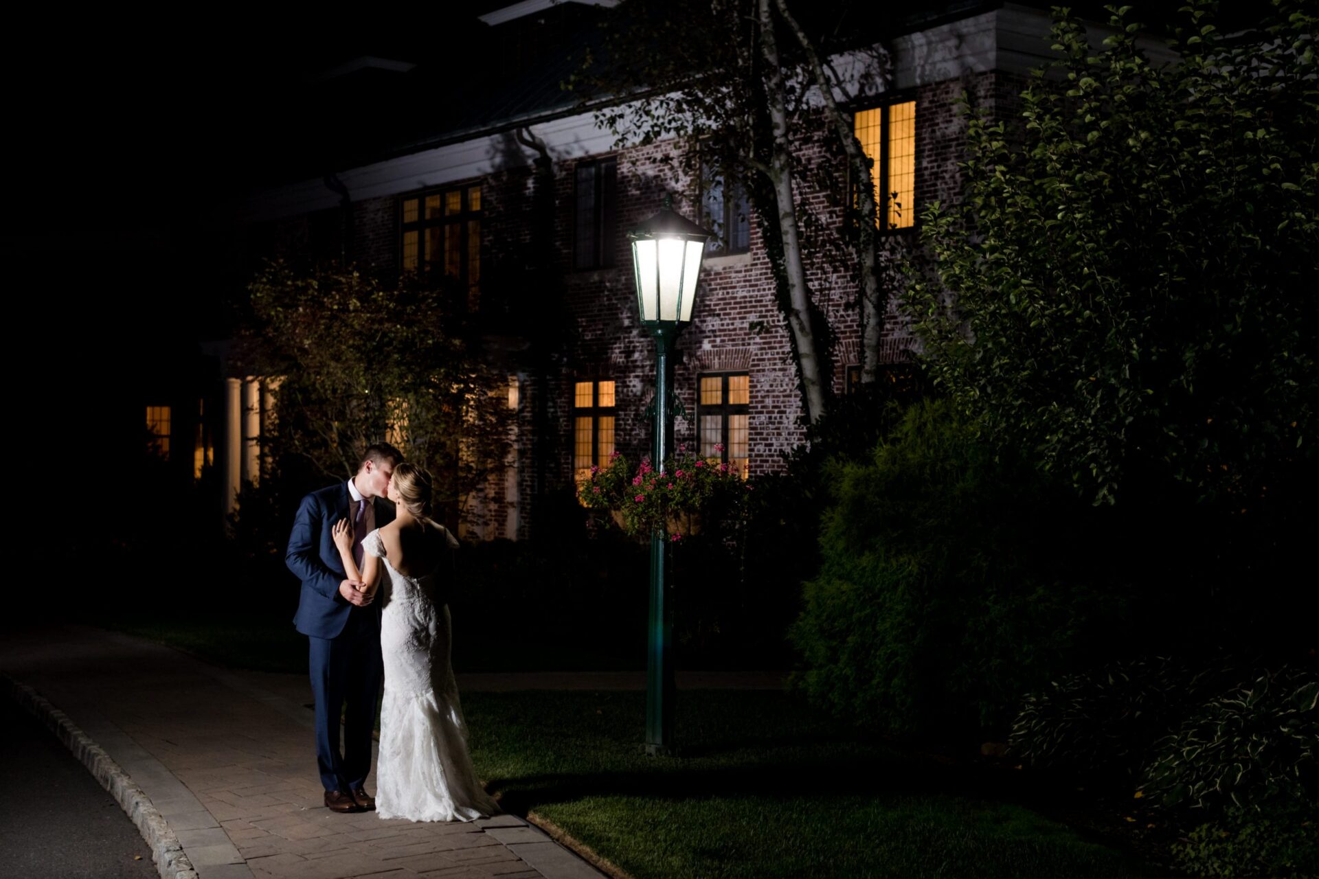 Couple kissing at night under a lamppost outside a brick clubhouse