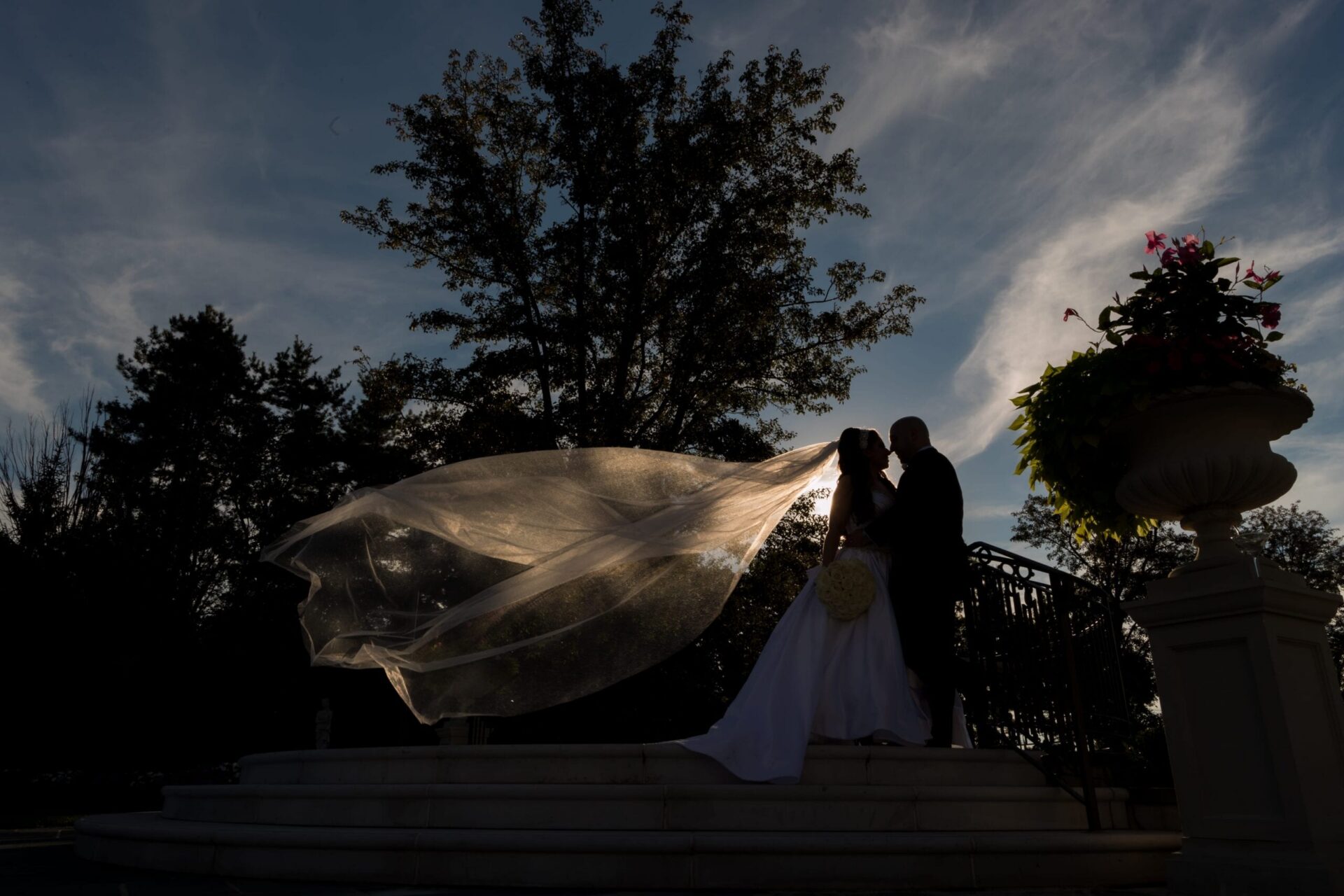 Silhouetted bride and groom at dusk on stone steps with her sheer veil blowing