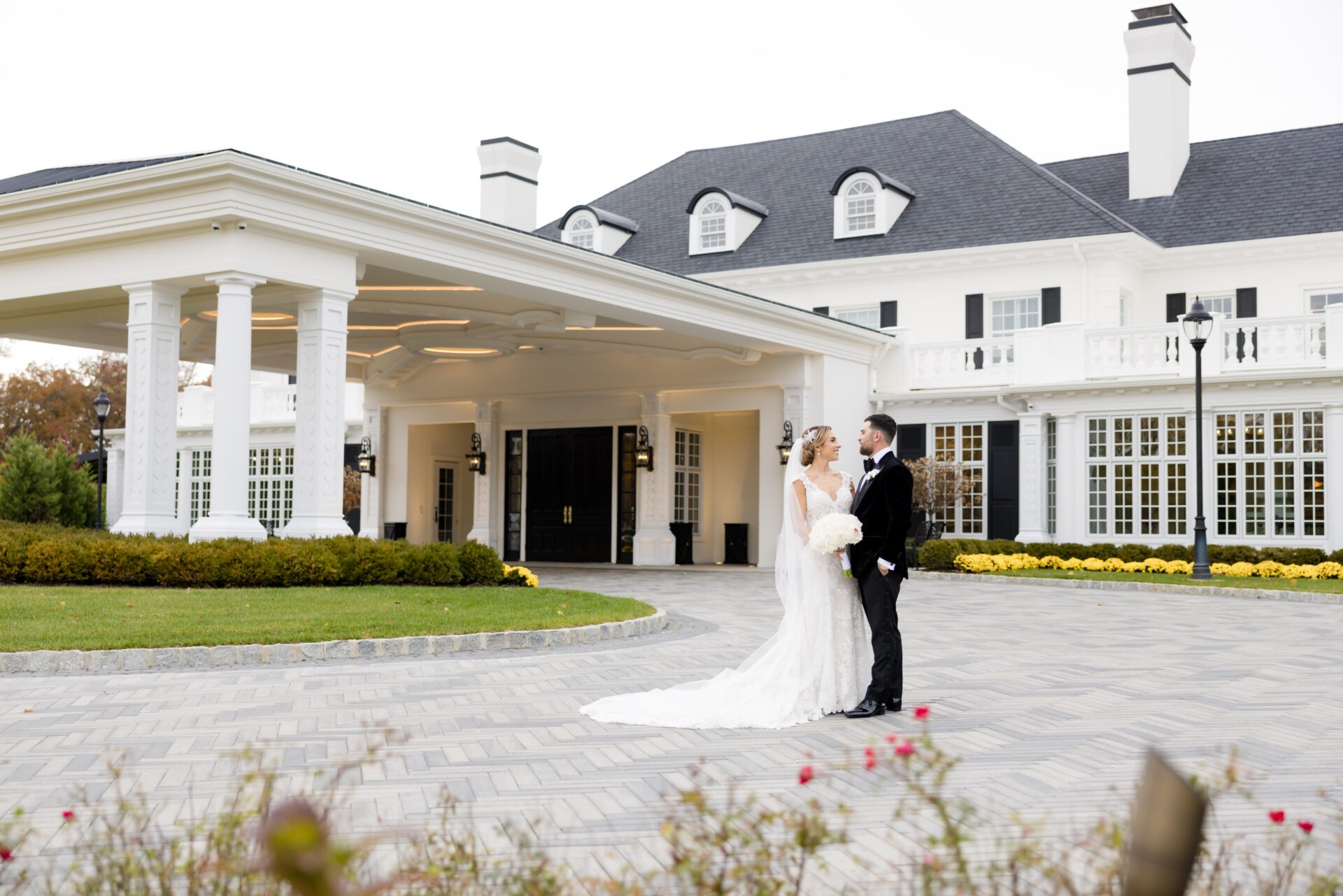 Bride and groom standing in front of the white Shadowbrook entrance with its covered portico
